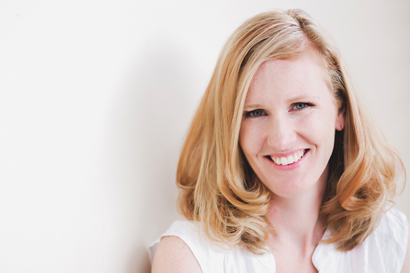 woman with red hair in white top leaning against a white wall