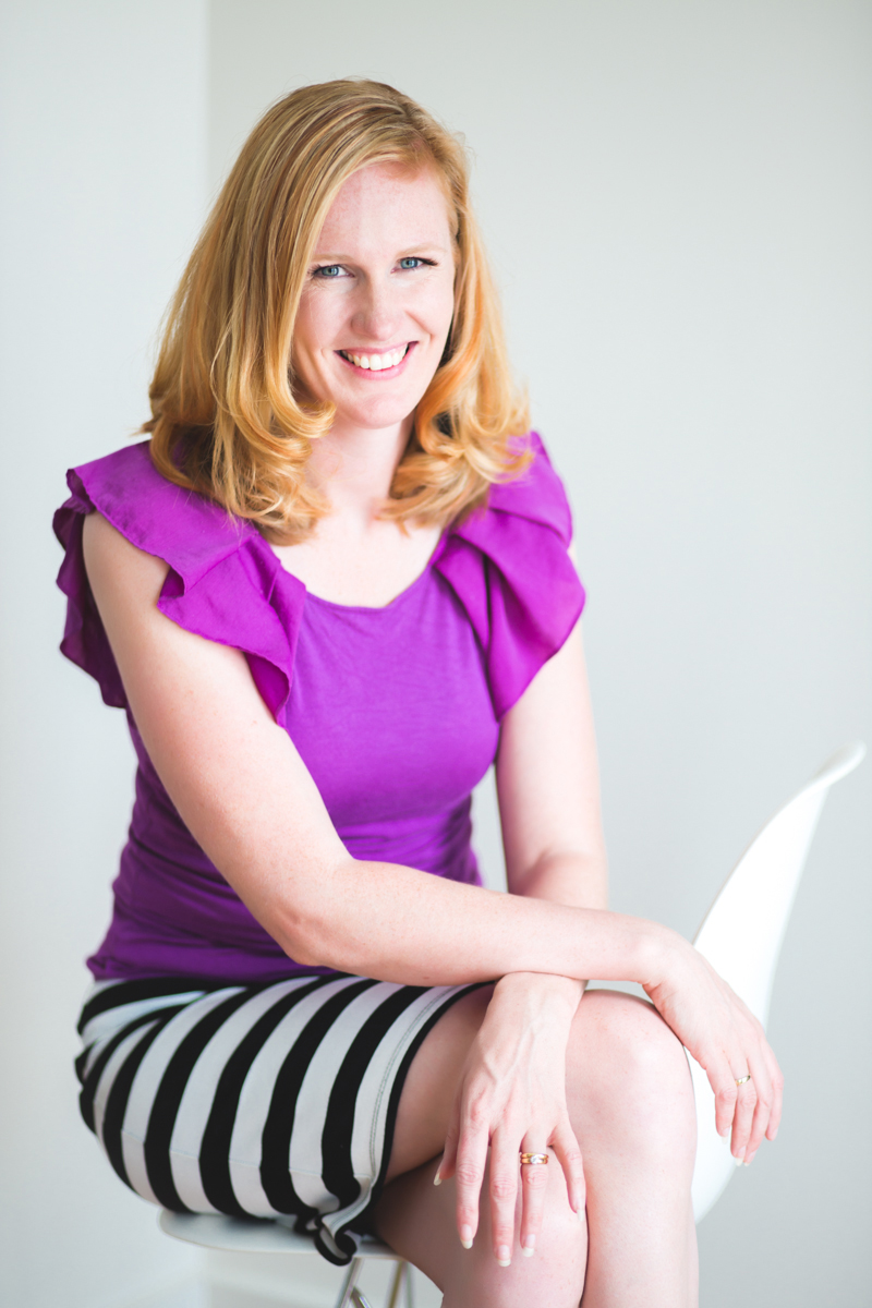 headshot of woman in purple top and striped skirt sitting on chair