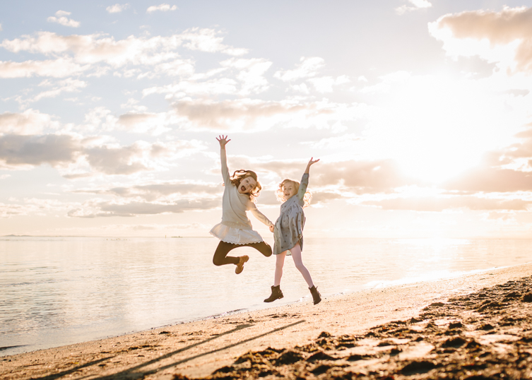 golden hour photography of two girls jumping on the beach 