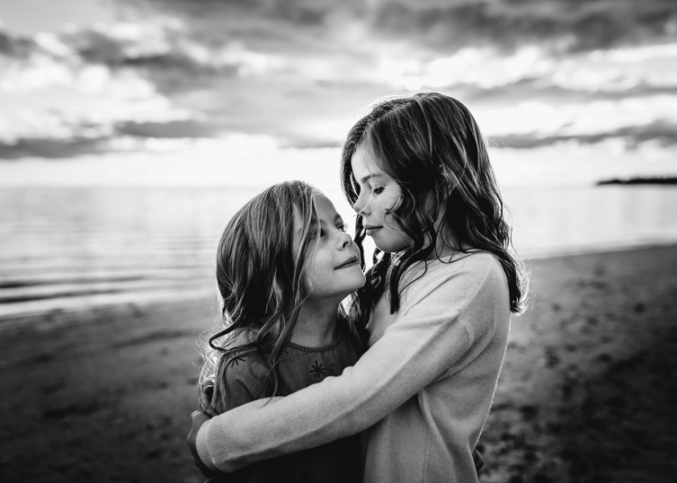 black and white photo of little girls hugging on the beach 