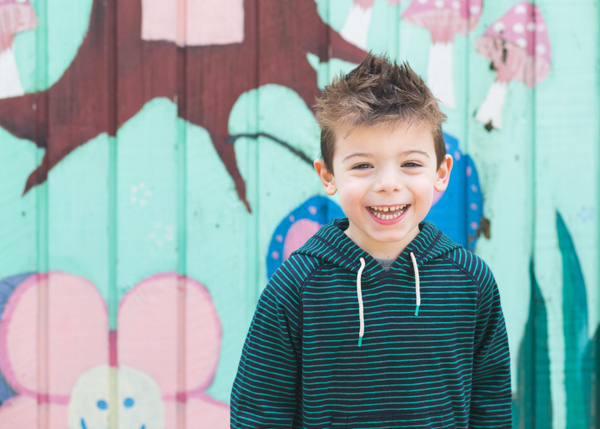 preschool boy laughing in front of wall mural
