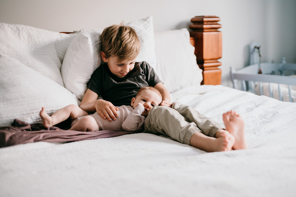 sibling and newborn in bed for a baby shoot