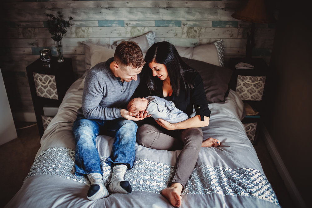 couple poses with baby sitting on bed