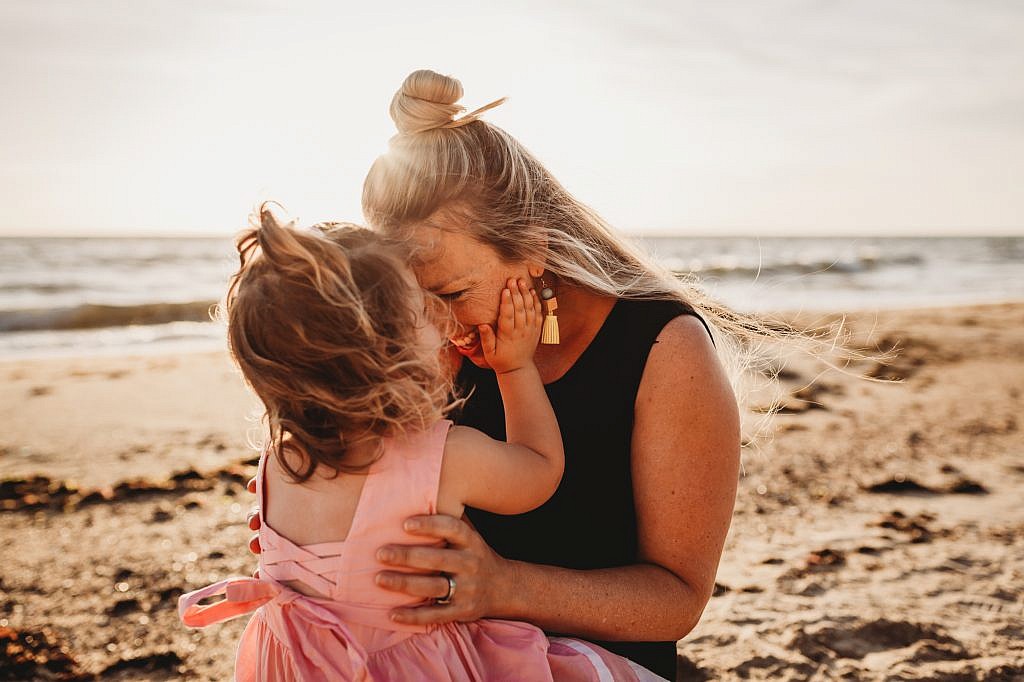 cute little girl at the beach holding her mother’s face