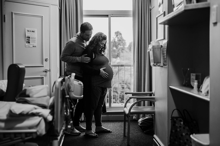 photo of man holding pregnant wife from behind before c-section