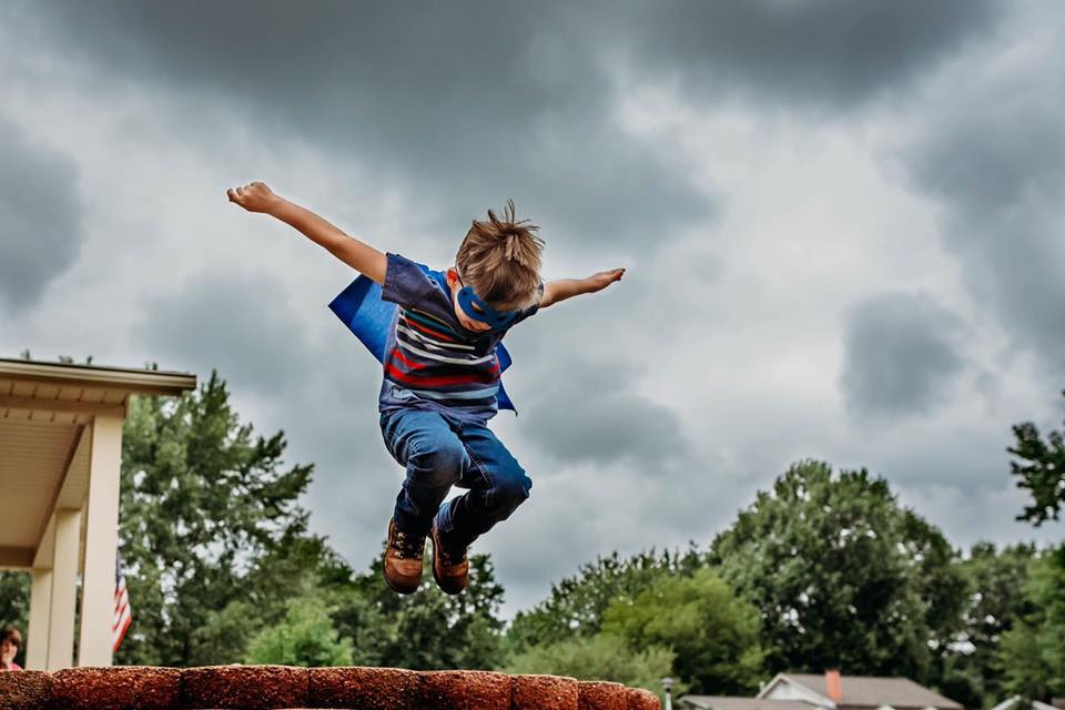 boy jumping wearing superhero cape