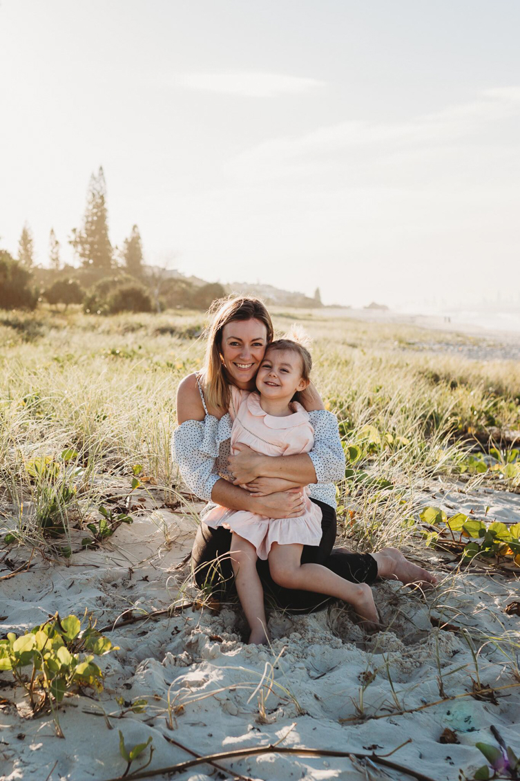 mother and daughter smiling and hugging at the beach