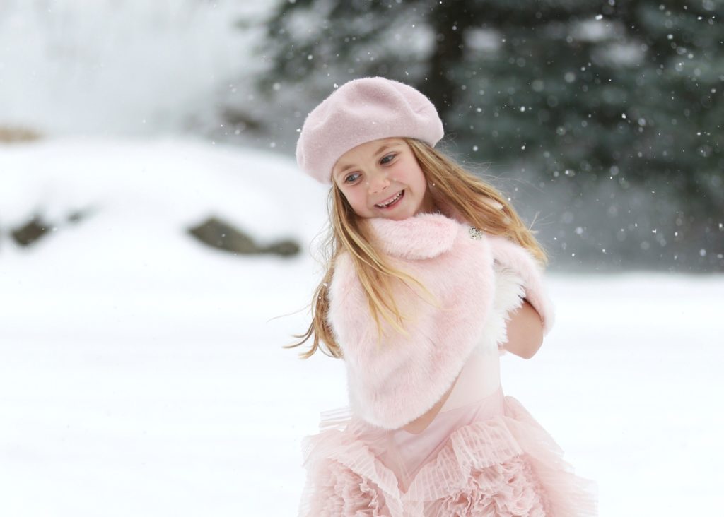 photography of girl dressed in a pink dress playing in the snow