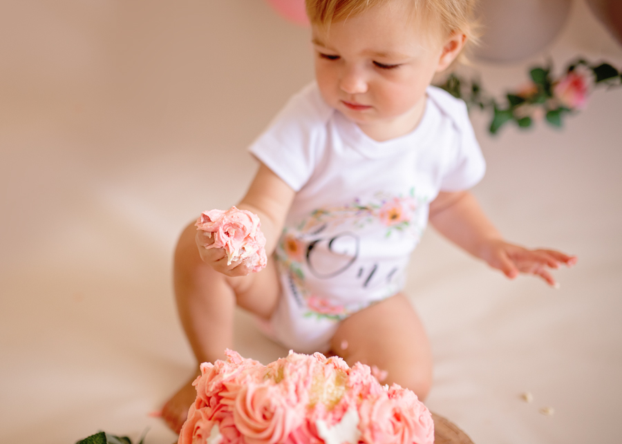 baby with cake in the hand during cake smash photoshoot