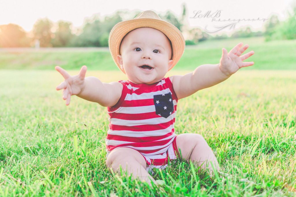 cute baby boy wearing a hat and sitting on grass wearing american flag