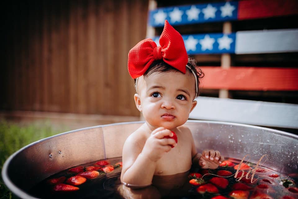 little girl in water with strawberries and american flag background
