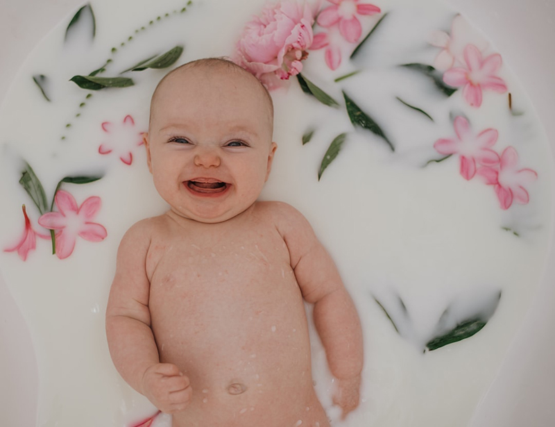 gorgeous baby smiling taking a milk bath surrounded by flowers