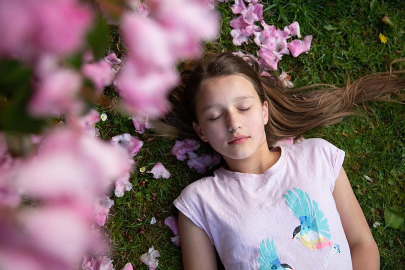 pink photography of girl lying on grass surrounded by pink flowers