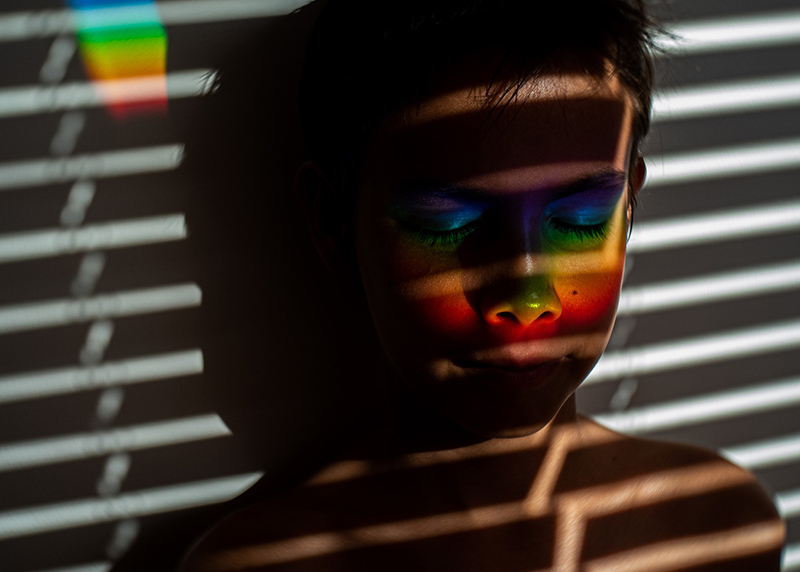boy in front of venetian blinds with rainbow on the face