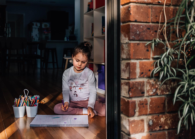 low light image of little girl drawing by the window