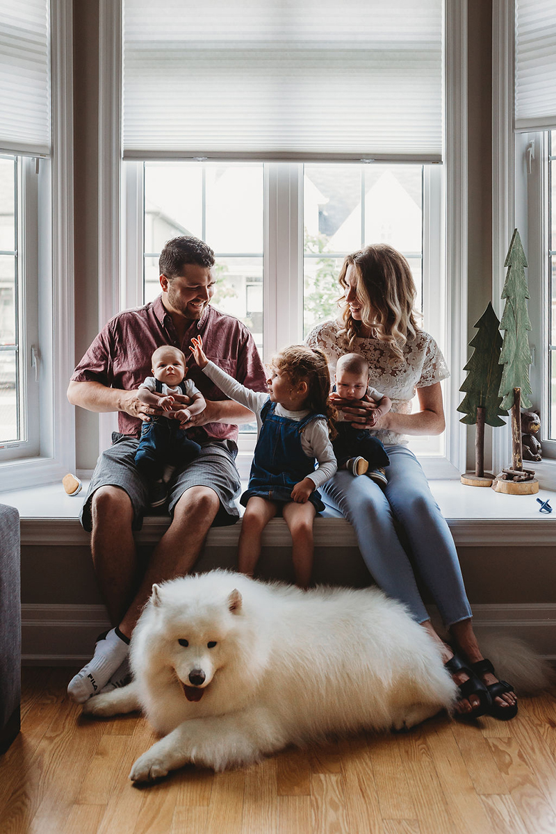 parents with little girl, newborn twins, and dog sitting by window