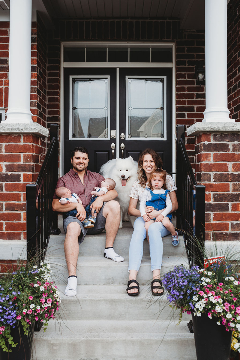 family with newborn babies, sibling, and dog in front of house 