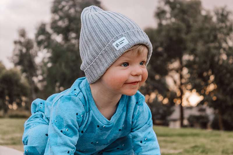 toddler boy wearing a blue sweater and grey hat in a park