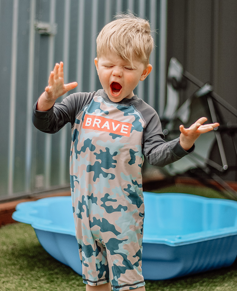 toddler boy wearing swim suit standing near a small swimming pool