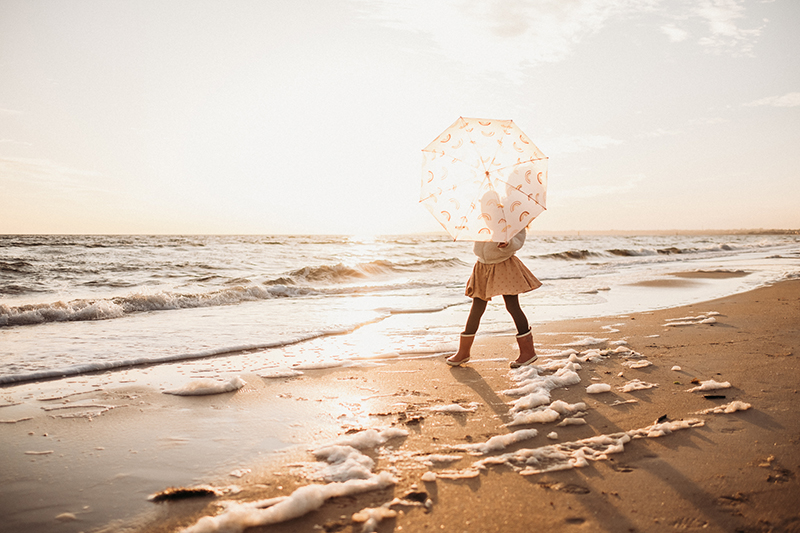 backlit photos of kid at the beach holding an umbrella
