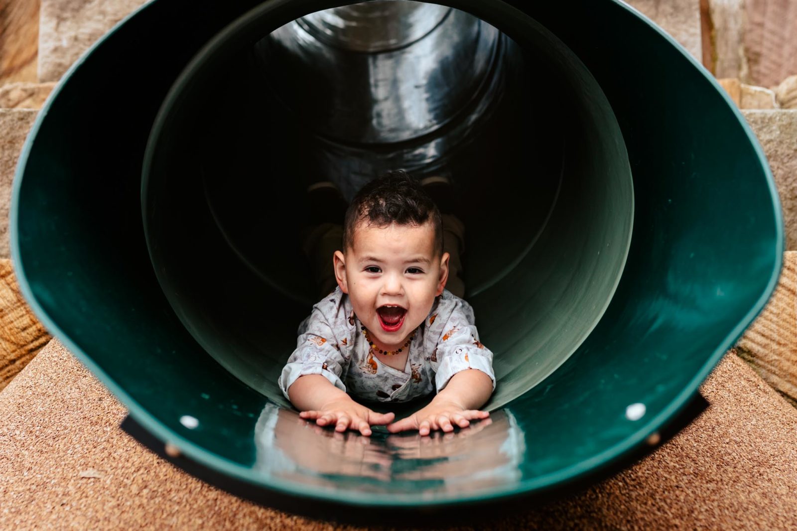 Toddler boy combing down a tube slide laughing