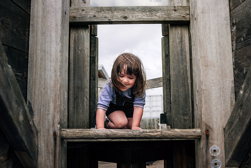 girl climbing through wooden structure at the park
