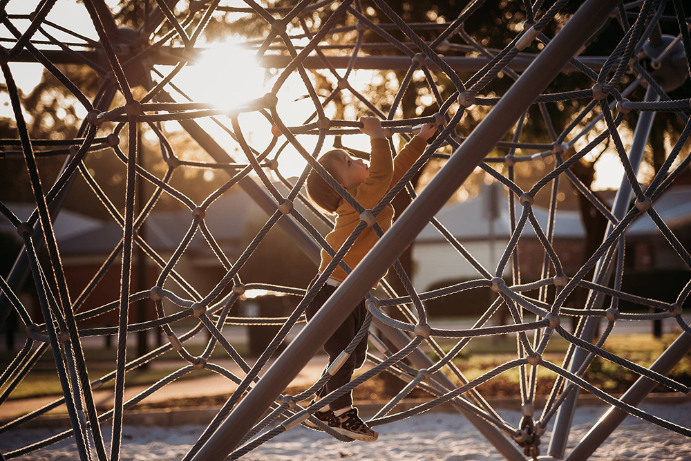 young boy climbing playground equipment in golden hour light