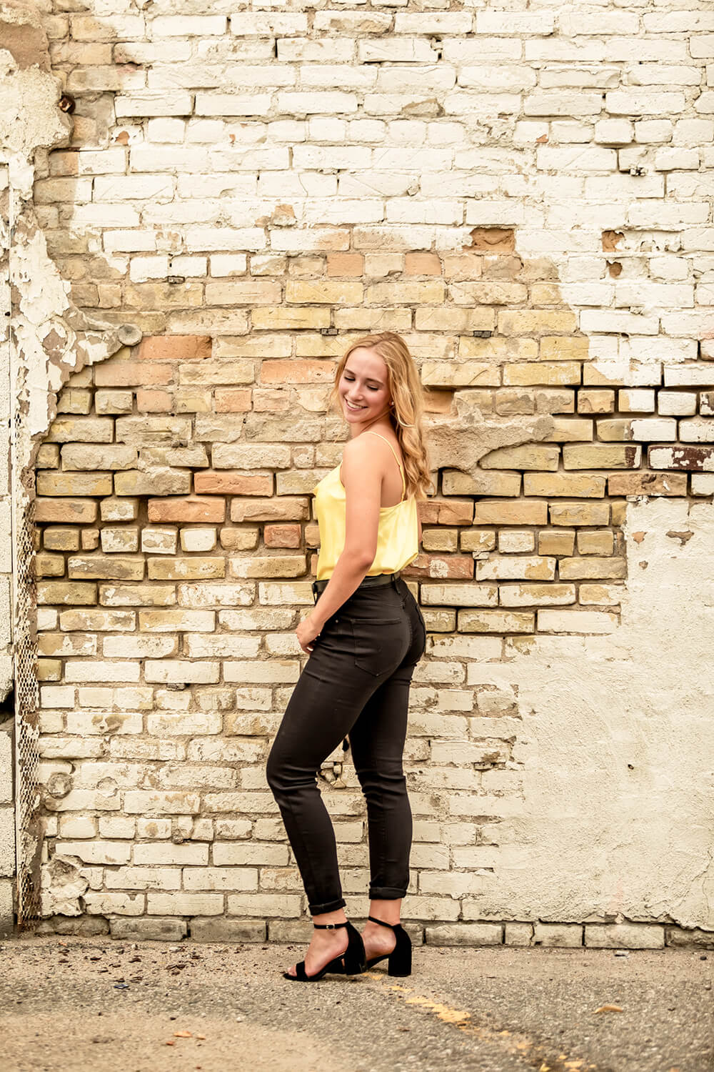 teenage girl posing in front of an urban wall side on wearing black jeans