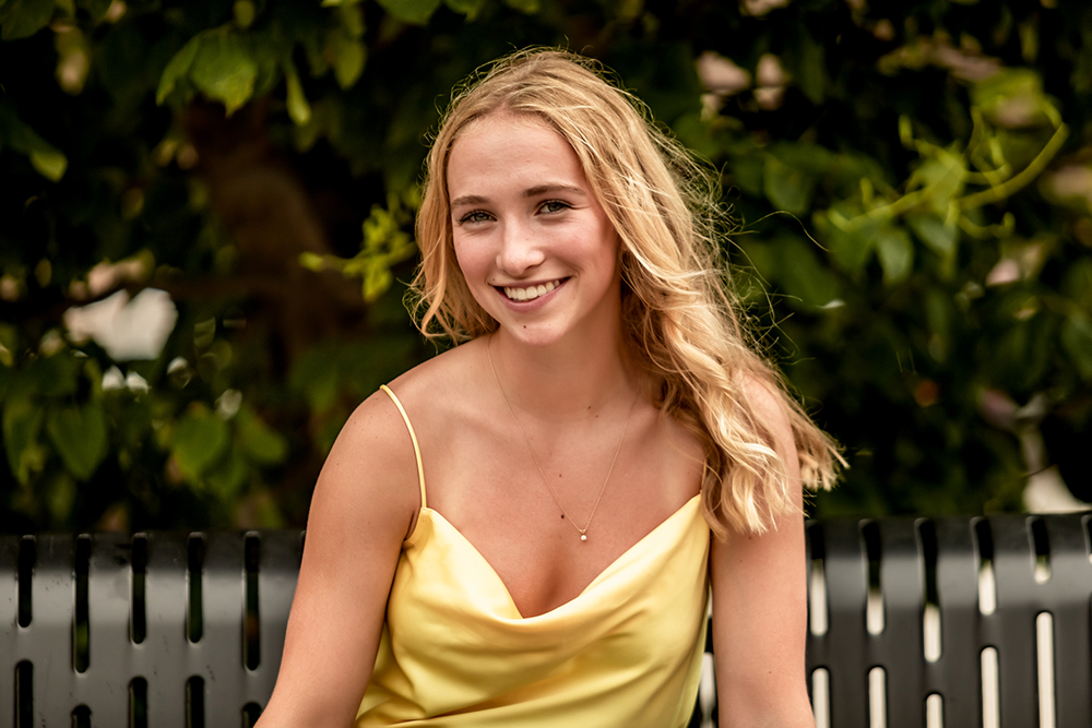 girl poses with long blonde hair at a grads photography session sitting on a park bench