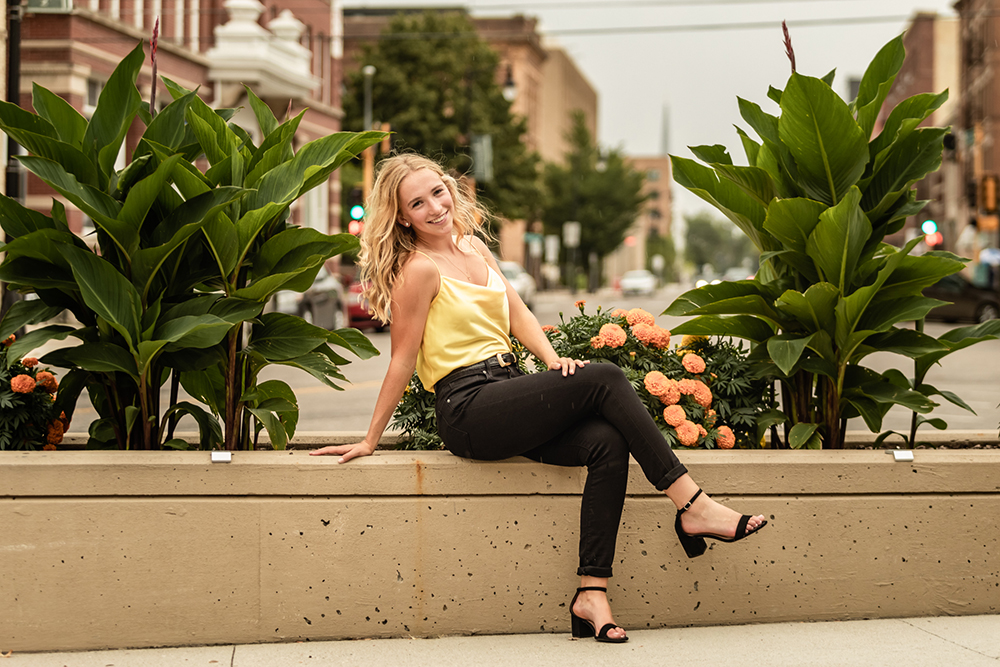 teenage girl posing on low wall in yellow shirt and black jeans