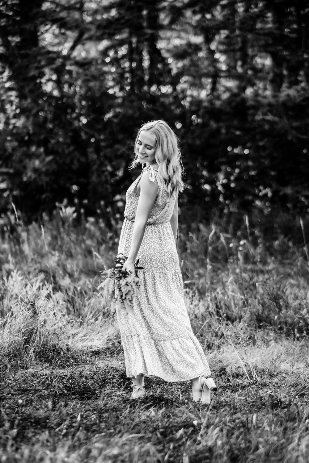 black & white photo of a girl in a field walking away and holding flowers