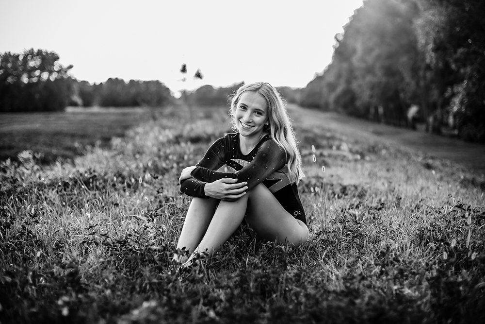 Grads photography session with a teenage girl sitting in a field with her arms wrapped around her knees