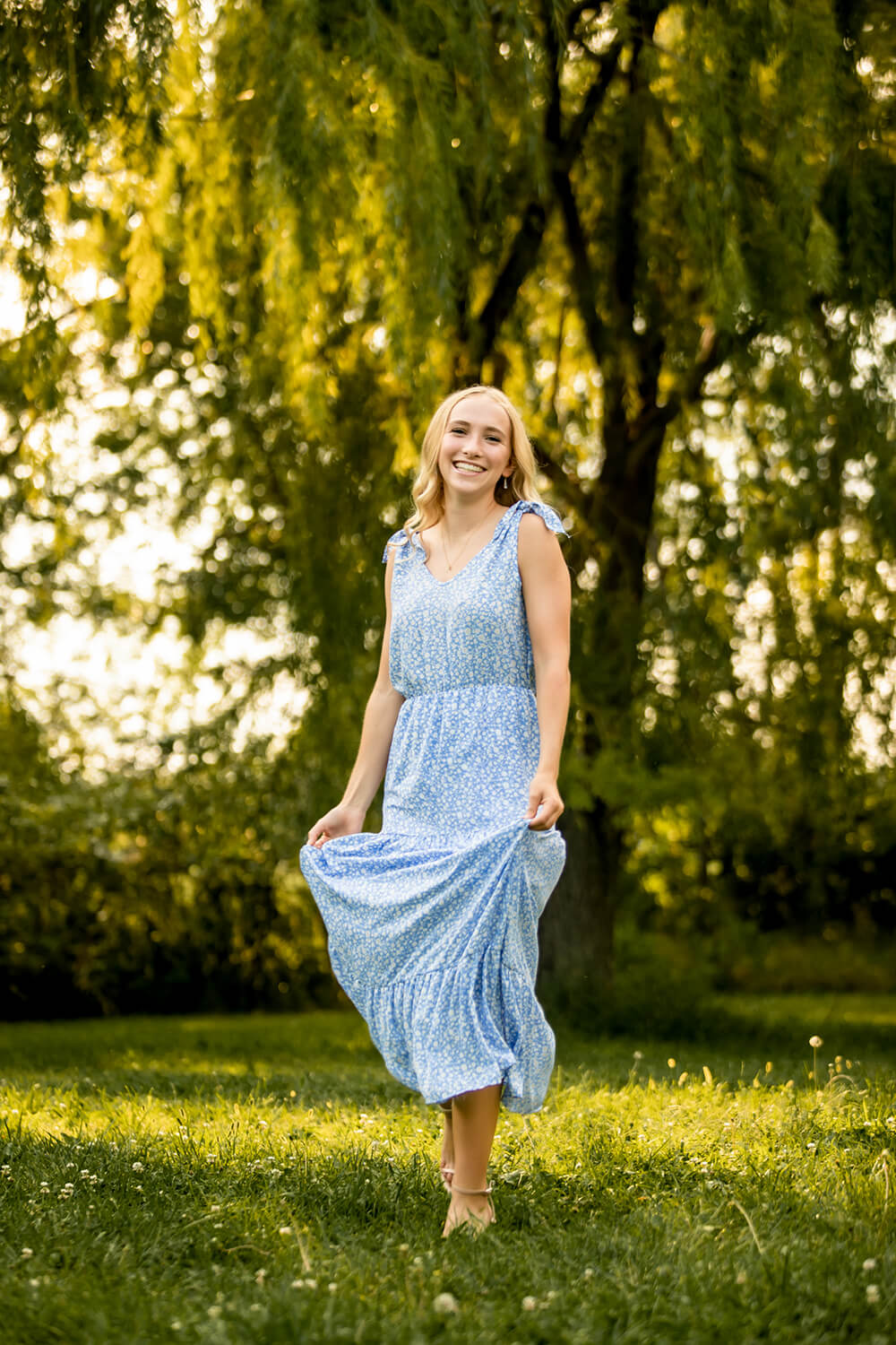 girl poses with blonde hair in a field wearing a blue dress