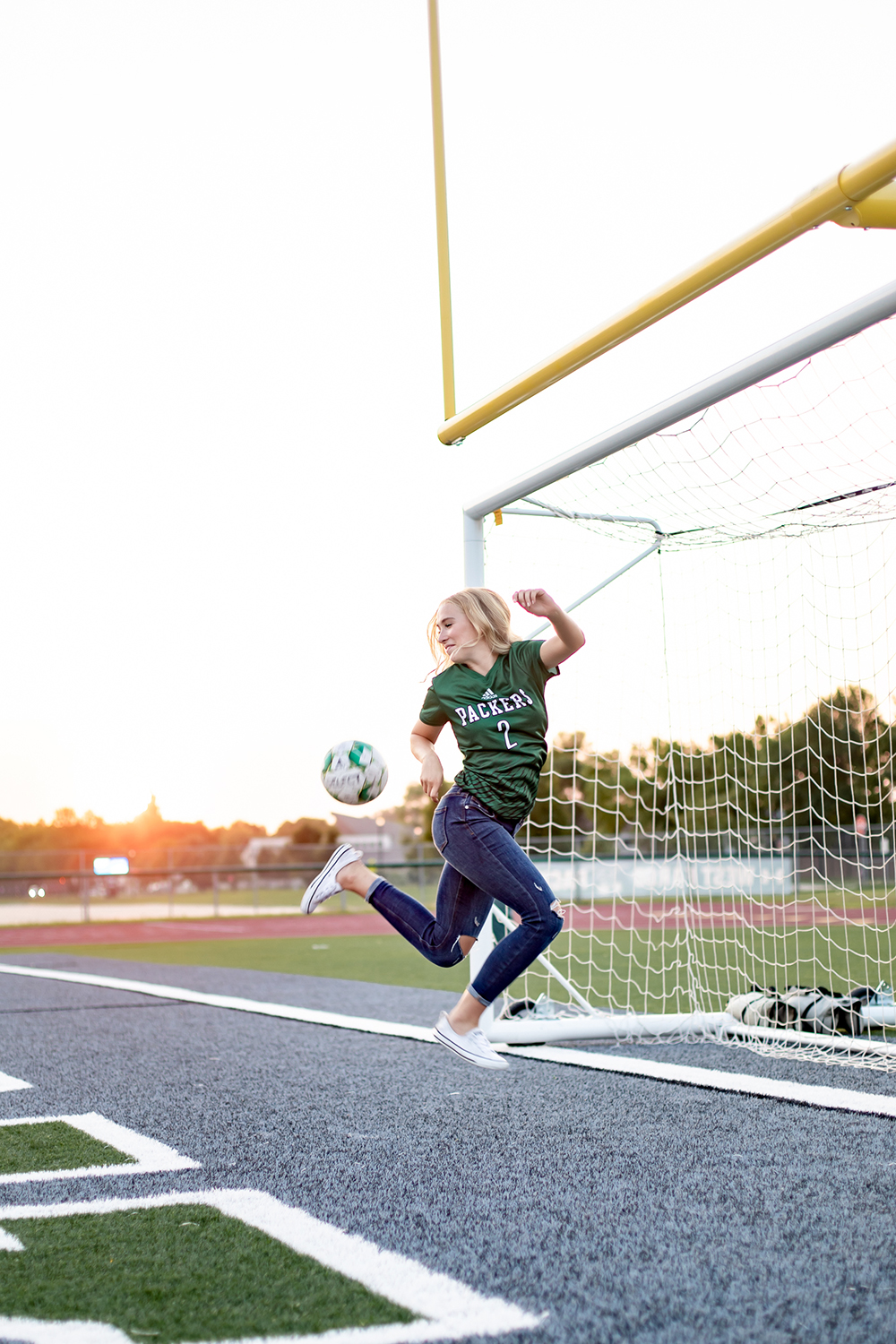 girl in midair kicking a soccer ball and wearing a green tshirt