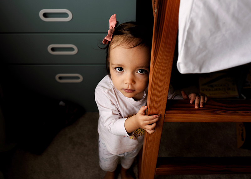 toddler girl in a bedroom leaning against a ladder