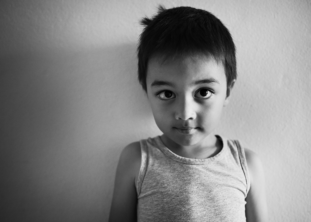 B&W portrait of a young boy against a white wall