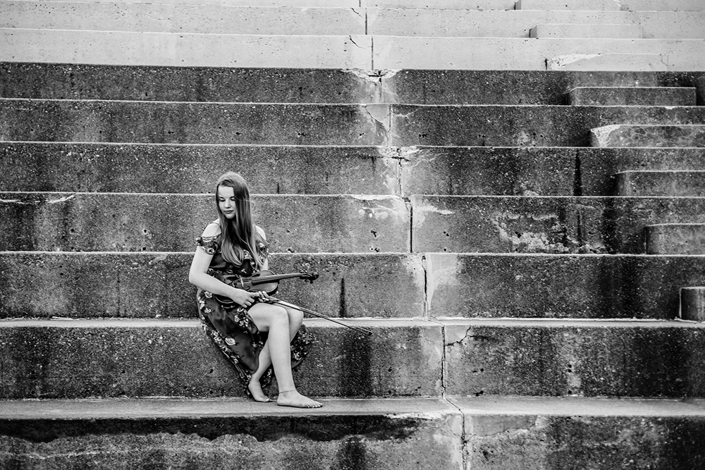 senior girl poses on steps holding a violin