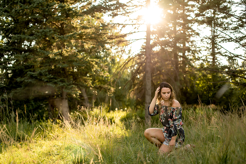 grads photography session photo of a teenage girl kneeling in a field with the sun behind her