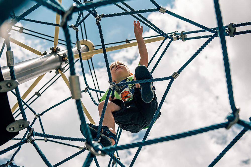 boy climbing playground rope structure at a park
