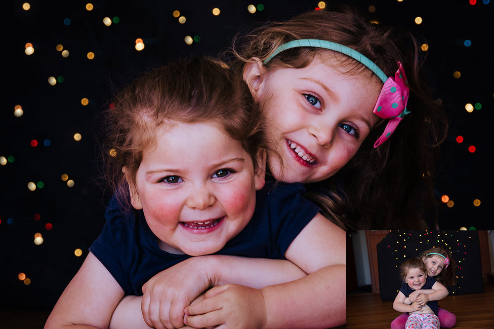 young sisters hugging and smiling with fairy lights in background