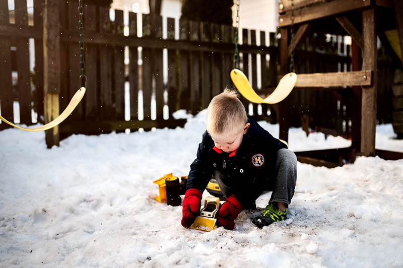 small boy playing with trucks in the snow