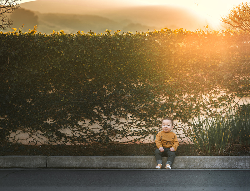 toddler boy sitting on kerb with backlighting