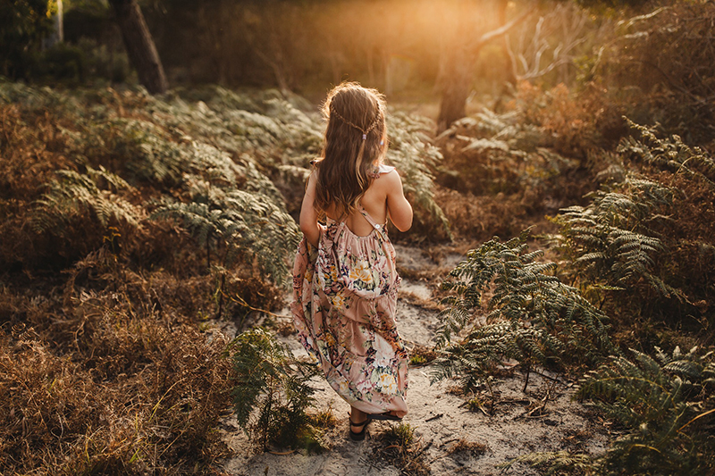 young girl in floral dress walking on a sandy path 