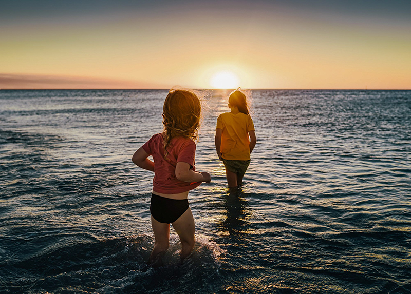 two girls in water at beach sunset