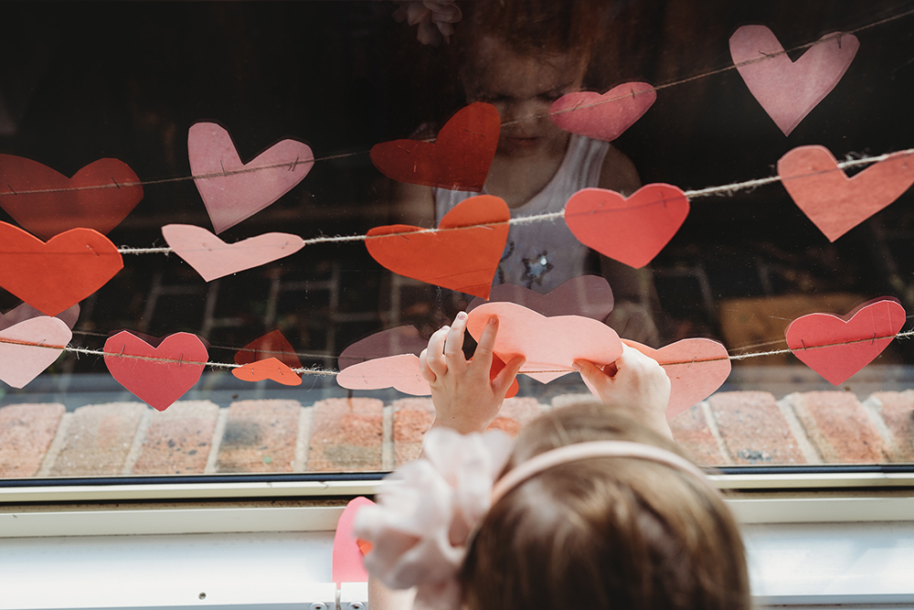 young girl hanging paper hearts in window