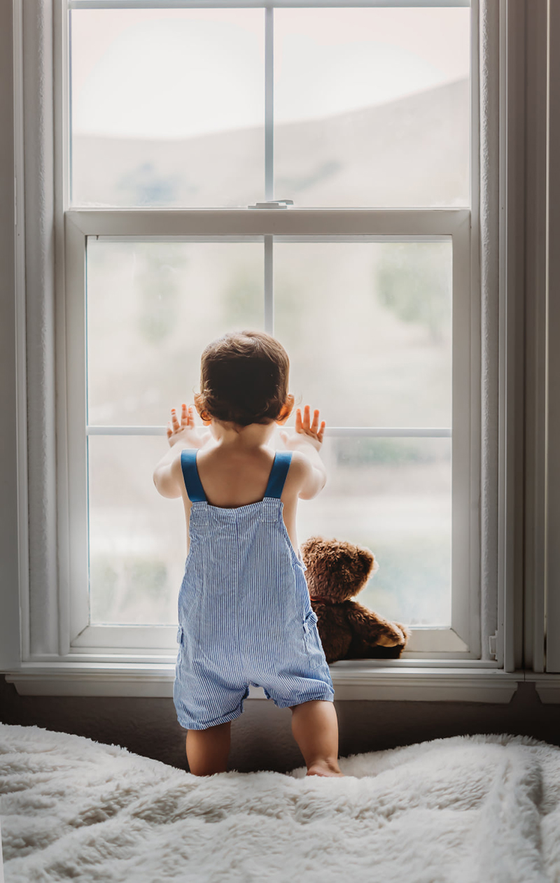 baby boy standing in front of a window with hands on the glass