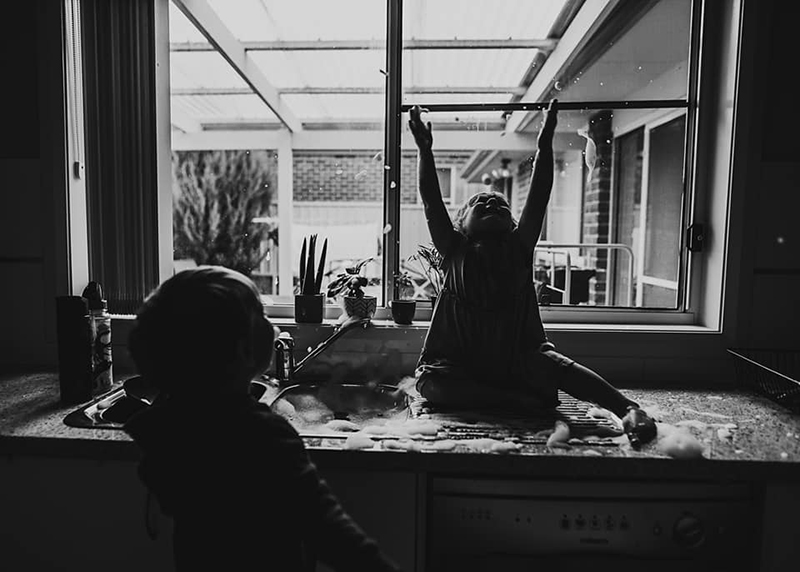 toddler girl sitting on a kitchen bench in front of a window backlit