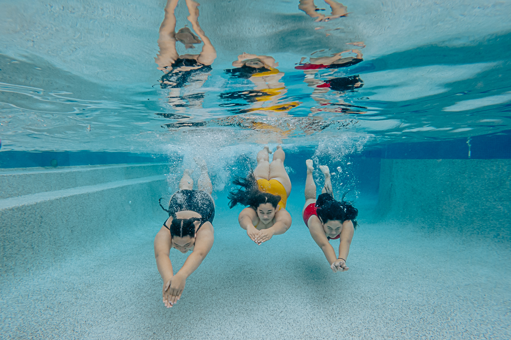 Three girls swimming underwater in a pool