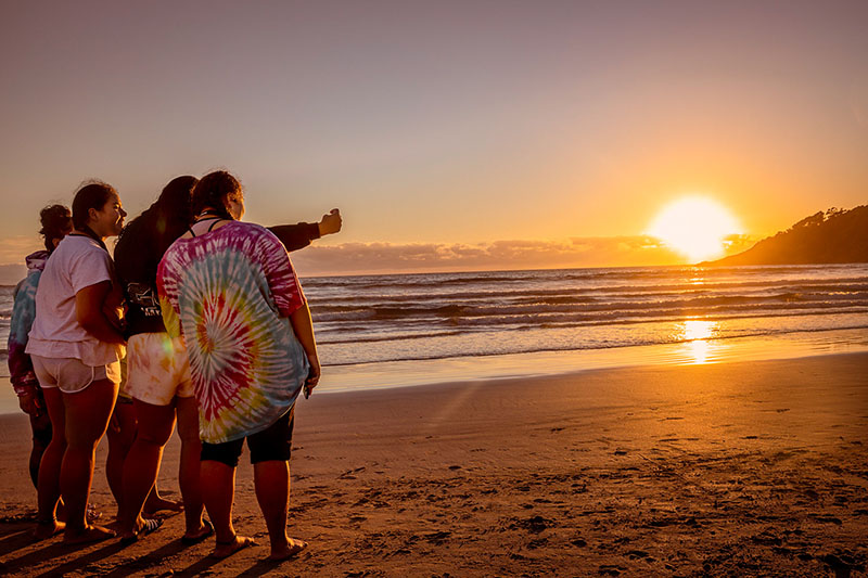 group of teenage girls standing on the beach at sunset