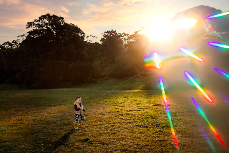 toddler boy flying kite with rainbow sunflare